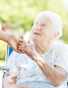 Senior woman in a wheelchair outside holding hands with her caretaker